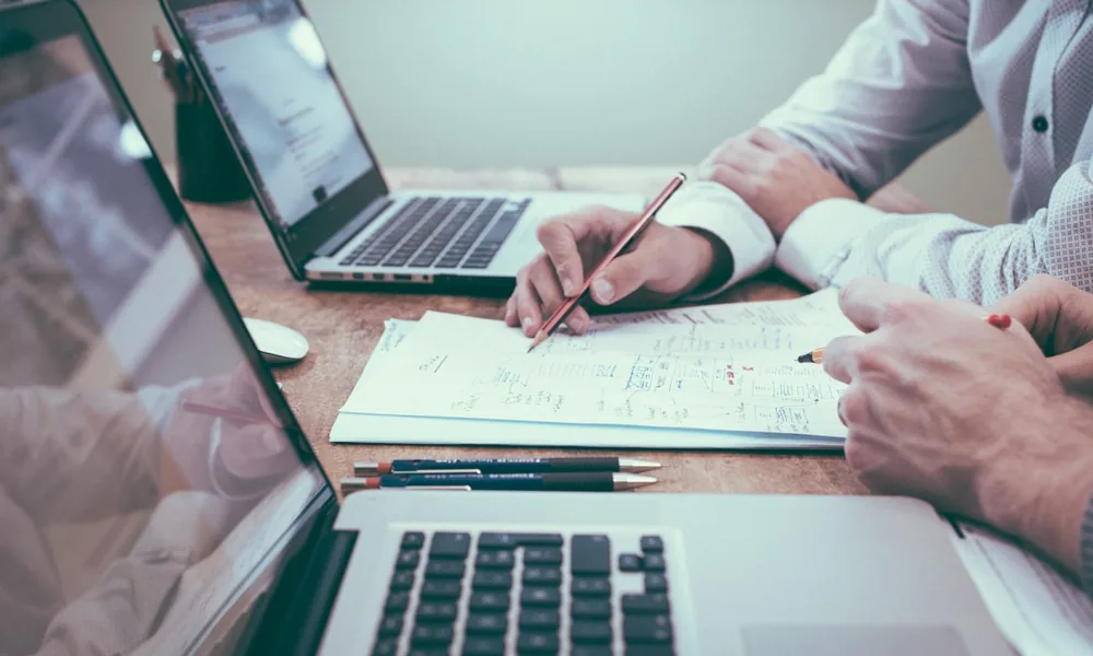 Two business owners reviewing invoice finance figures at a desk with a laptop and calculator