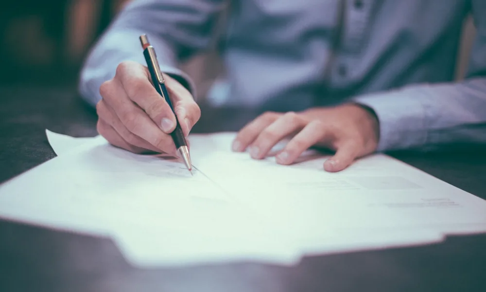 A hand signing a finance agreement, weighing up recourse and non-recourse terms